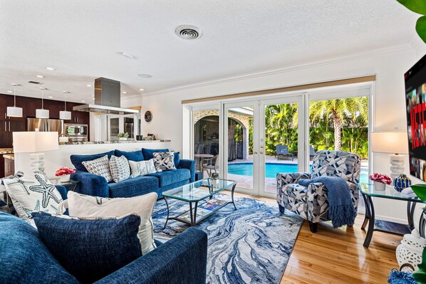 A modern living room with a blue sofa, a glass coffee table, and a poolside view.