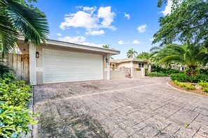A residential property with a garage, paved driveway, and lush greenery.