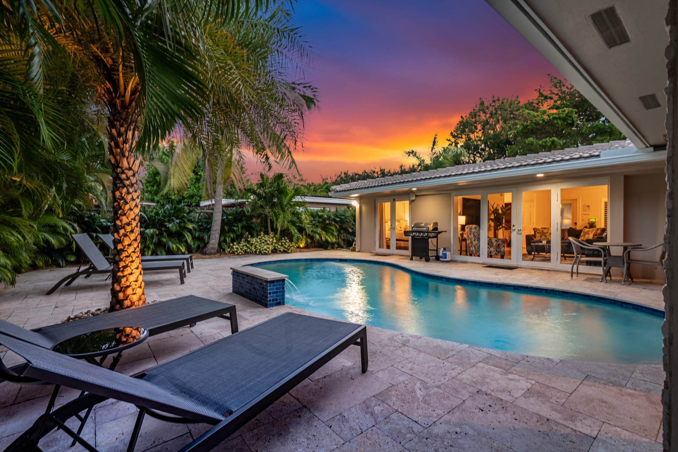 Une piscine avec des chaises longues, un palmier et une maison dotée d’un patio.