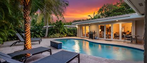 Una piscina con sillas de descanso, una palmera y una casa con un patio.