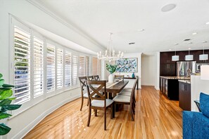 Una cocina moderna con comedor, suelo de madera y ventanas grandes con persianas.