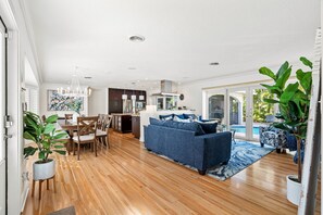 A spacious living area with a blue sofa, wooden flooring, and a view of a pool.