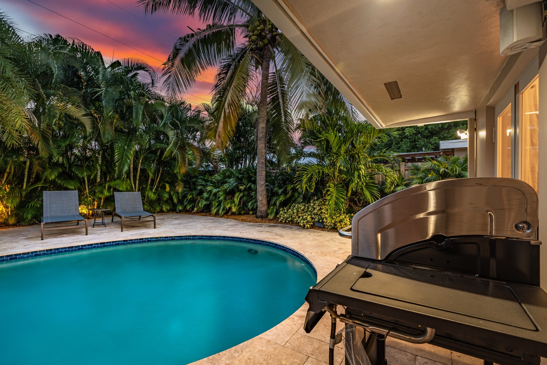Una piscina con zona de parrilla, rodeada de palmeras y vistas al atardecer.