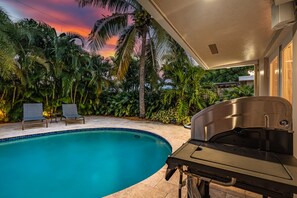 Una piscina con zona de parrilla, rodeada de palmeras y vistas al atardecer.