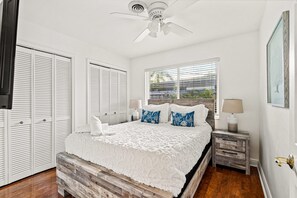 A bedroom with a bed, bedside tables, a ceiling fan, and a window with blinds.