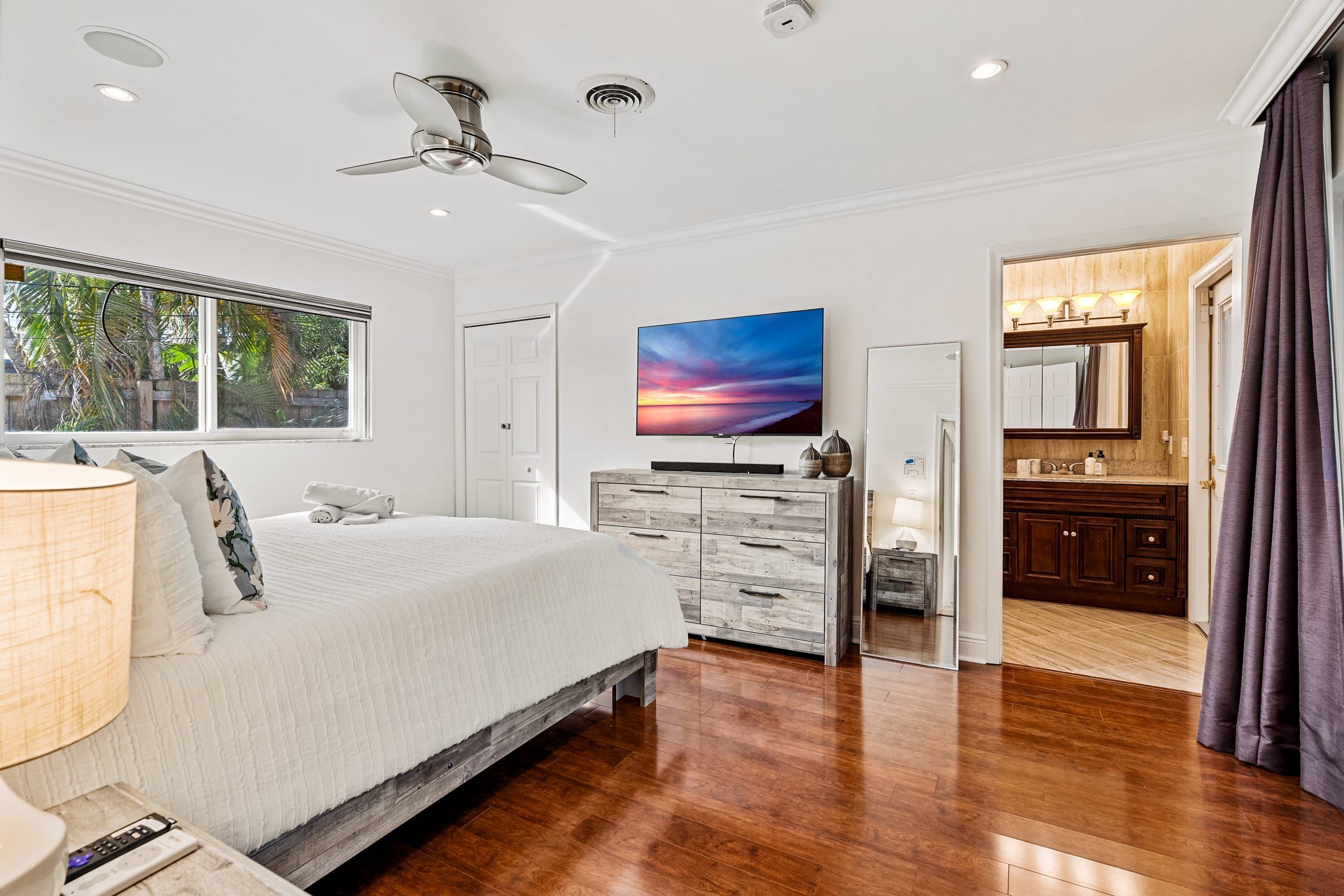 Ein Schlafzimmer mit Bett, Fernseher, Kommode, Schminktisch und Deckenventilator.