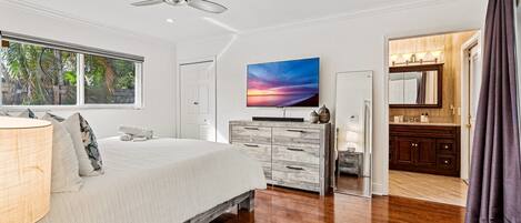 Ein Schlafzimmer mit Bett, Fernseher, Kommode, Schminktisch und Deckenventilator.
