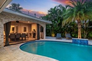 A poolside area with a curved pool, outdoor seating, and a covered patio.