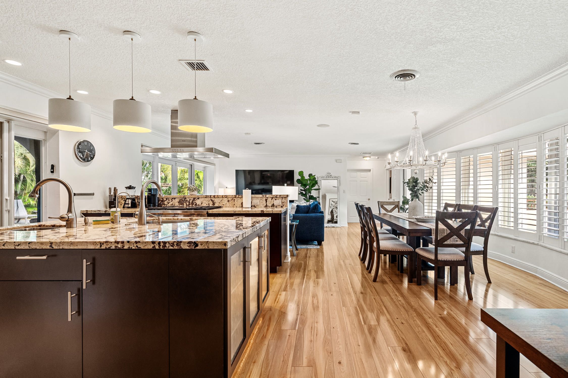 A modern kitchen with a large island, pendant lighting, and a dining area with a wooden table and chairs.