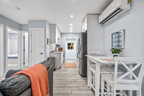 A modern kitchen with white cabinetry, a dining table with white chairs, and a visible refrigerator.