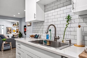 Una cocina moderna con armarios blancos, un lavamanos de acero inoxidable y una planta de bambú.