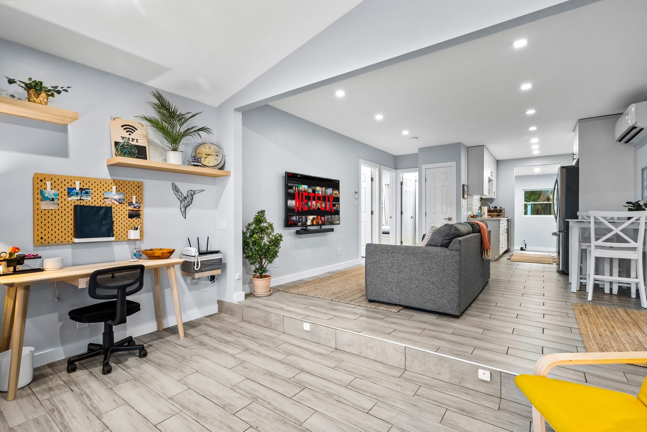 Een moderne woonkamer met een grijze bank, een houten bureau en een televisie waarop Netflix wordt afgespeeld.