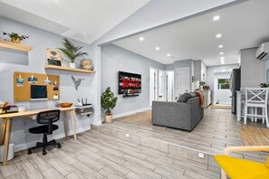 Una sala de estar moderna con un sofá gris, piso de madera, un escritorio con una computadora y un televisor que muestra el logotipo de Netflix.