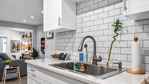 A modern kitchen with white cabinets, a stainless steel sink, and a tiled backsplash. - Zen Retreat - Sauna, Pool, Cold Plunge & More! (Fort Lauderdale)