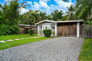A house with a gravel driveway, a wooden fence, and lush greenery.