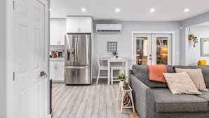 A modern kitchen with stainless steel appliances, a dining area with a white table and chairs, and a grey sofa with cushions. - Zen Retreat - Sauna, Pool, Cold Plunge & More! (Fort Lauderdale)