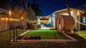 A well-lit outdoor area with a wooden barrel, a hot tub, and exercise equipment. - Zen Retreat - Sauna, Pool, Cold Plunge & More! (Fort Lauderdale)