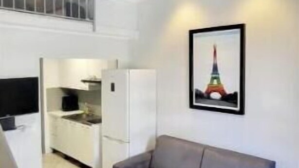 Un salon moderne avec un canapé gris, une table basse blanche et une cuisine en arrière-plan.