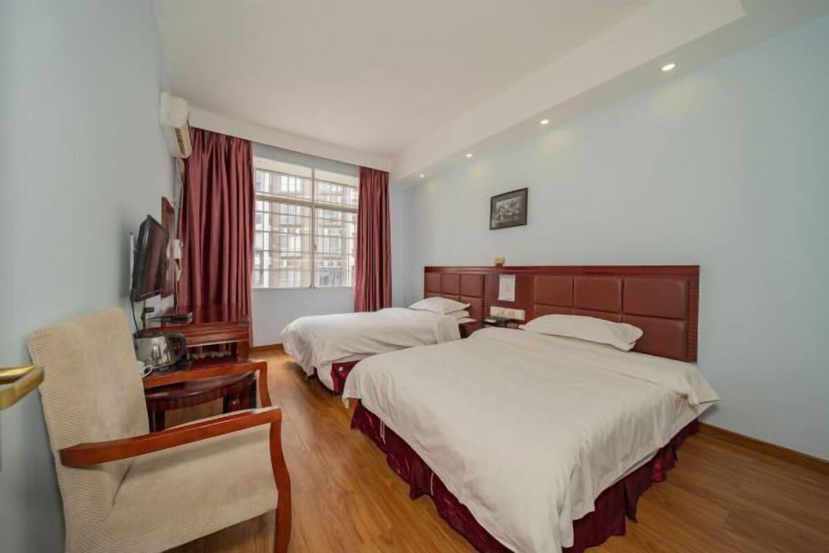 A hotel room with two beds, a desk with a chair, a television, and a window with curtains.