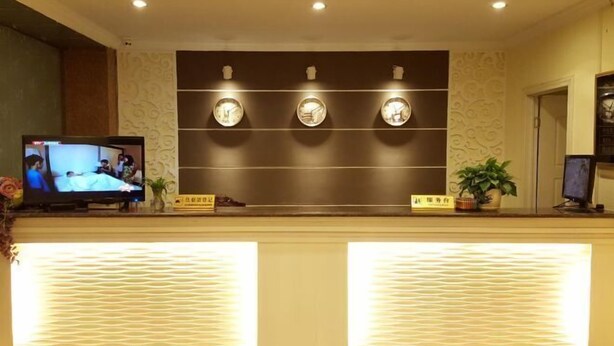 A hotel reception area with a television displaying a scene, three wall-mounted clocks, and a reception desk with a decorative plant. - Yongzhou Haolaiwu Riverview Hotel (Yongzhou)