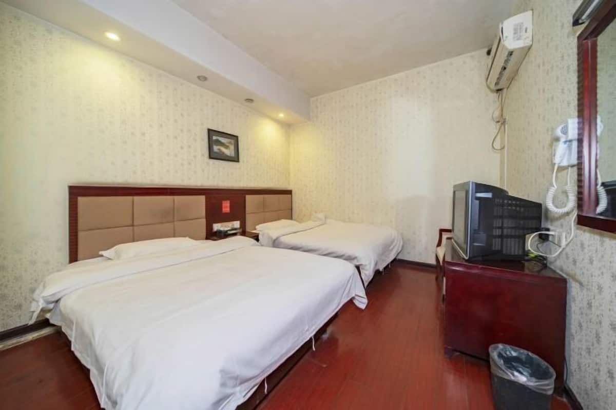 A hotel room with two single beds, a wooden headboard, a television, and a waste bin.