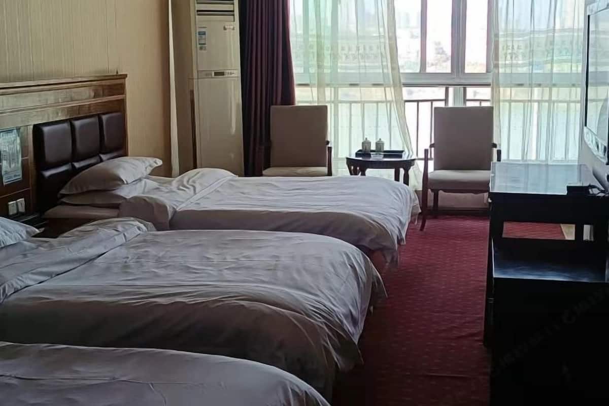 A hotel room with three beds, a desk, chairs, and a large window with a view.