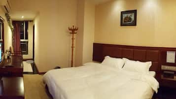 A hotel room with a large bed, a wooden headboard, a nightstand, and a coat rack.
