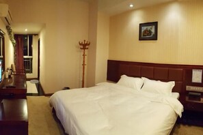 Habitación de hotel con una cama grande, cabecera de madera, mesita de noche y perchero.