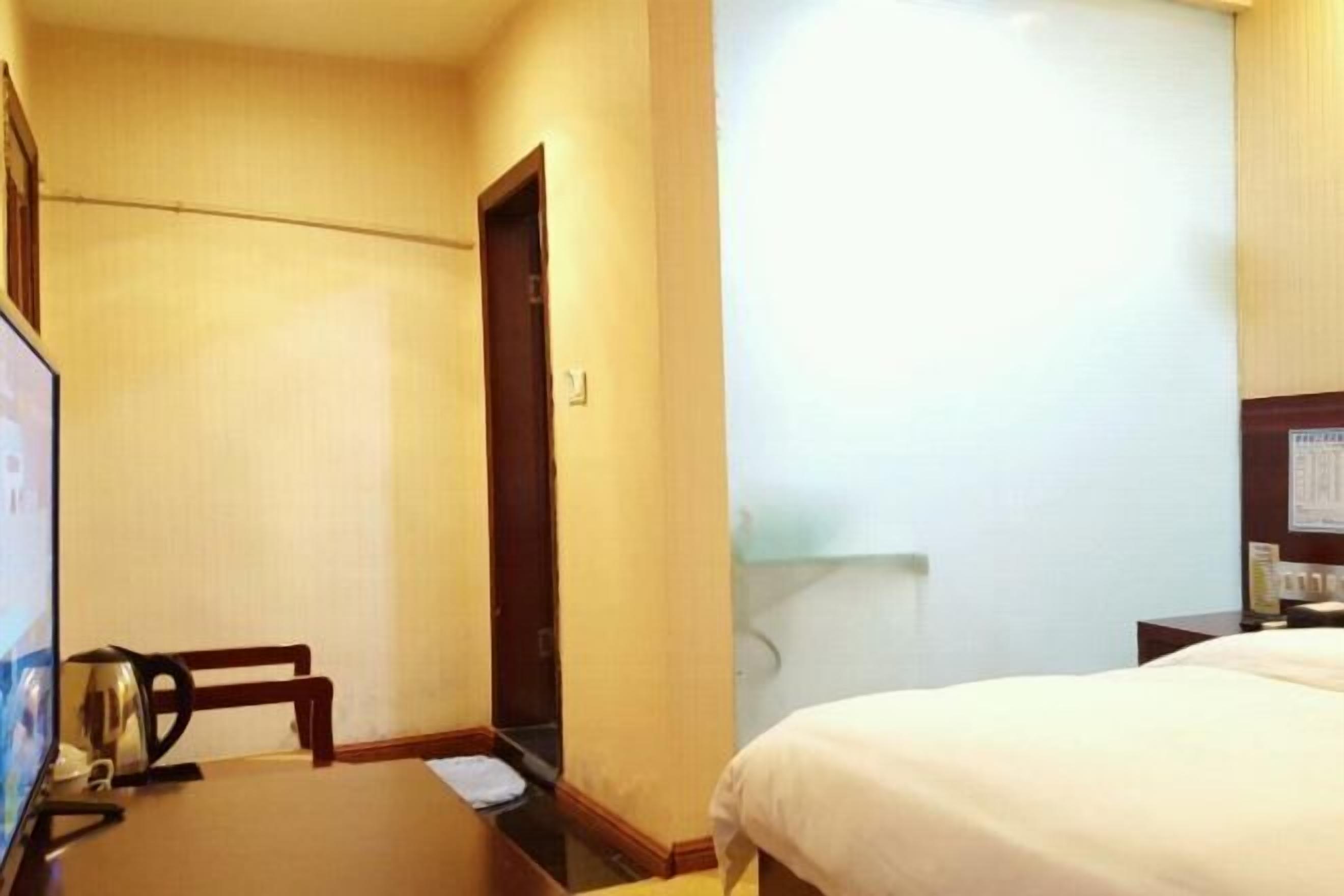 Habitación de hotel con cama, escritorio con silla, televisor y pequeña mesa con tetera.