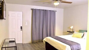 A bedroom with a bed, a ceiling fan, a door, and a small table. - Chayo's Departamentos (Ensenada)