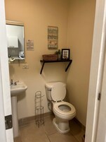 A small bathroom with a toilet, sink, and a shelf above the toilet.