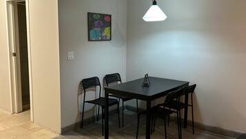 A dining area with a table and chairs, a hanging light fixture, and a door leading to another room.