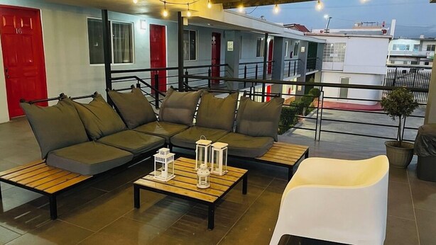 A modern outdoor seating area with a sofa, two wooden tables, and a white chair. - Chayo's Departamentos (Ensenada)