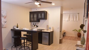 A compact kitchen with a bar area, a ceiling fan, and a dining area with a blue sofa. - Chayo's Departamentos (Ensenada)