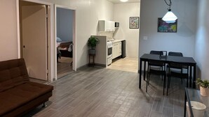 A living room with a brown sofa, a dining table with four chairs, and a kitchen area with a microwave, stove, and sink. - Chayo's Departamentos (Ensenada)