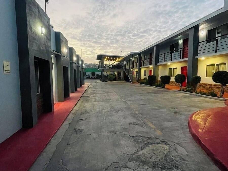 Un pasillo con varias habitaciones, cada una con una puerta y una ventana. Hay escalones que conducen a las habitaciones, y una alfombra roja recorre el pasillo.