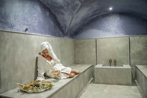 A person seated on a bench in a modern, dimly lit room with a unique ceiling design, holding a bowl and a tray with food items. - Al Destino Luxury Villa & Spa Marrakech (Oulad Hassoune)