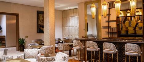 A hotel lobby with patterned sofas, a bar area with stools, and hanging lamps.