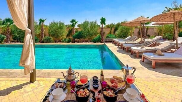 A poolside table with a meal setup, overlooking a swimming pool and lounge area. - Al Destino Luxury Villa & Spa Marrakech (Oulad Hassoune)