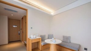 Una habitación de hotel moderna con un banco de madera, una pequeña mesa redonda y una puerta que da a otra habitación.