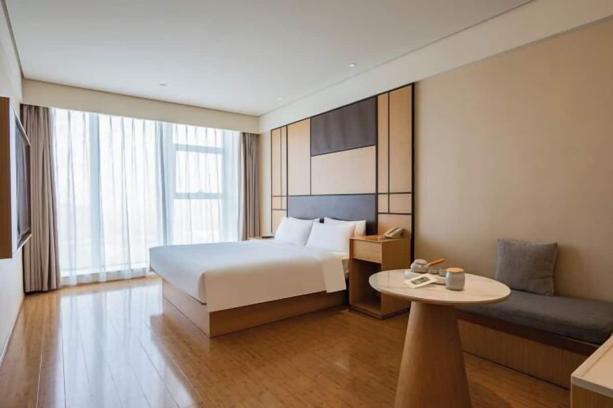 A modern hotel room with a large bed, bedside table, and a seating area.