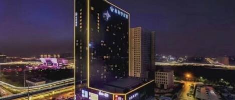Un immeuble de grande hauteur, doté d’une enseigne lumineuse, situé dans un quartier urbain animé, entouré de rues et d’autres bâtiments.