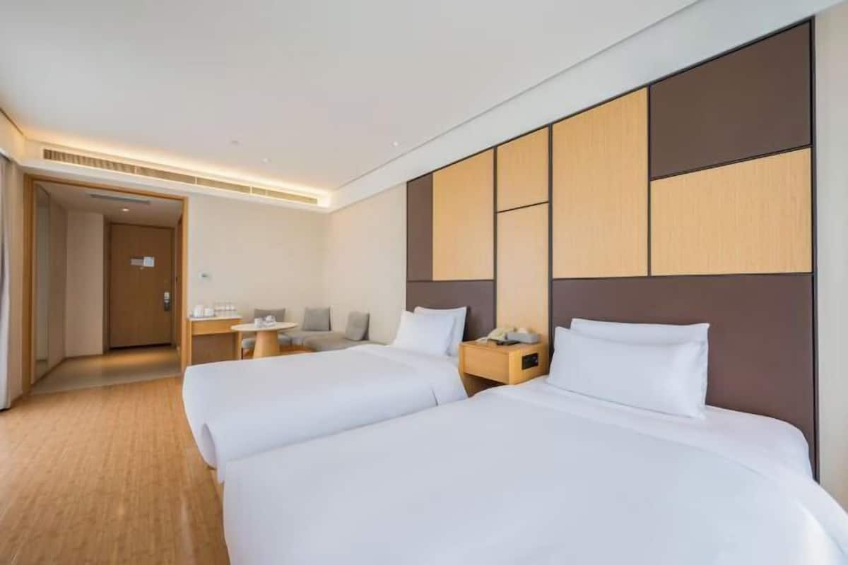 A hotel room with two beds, a desk, and a small seating area.