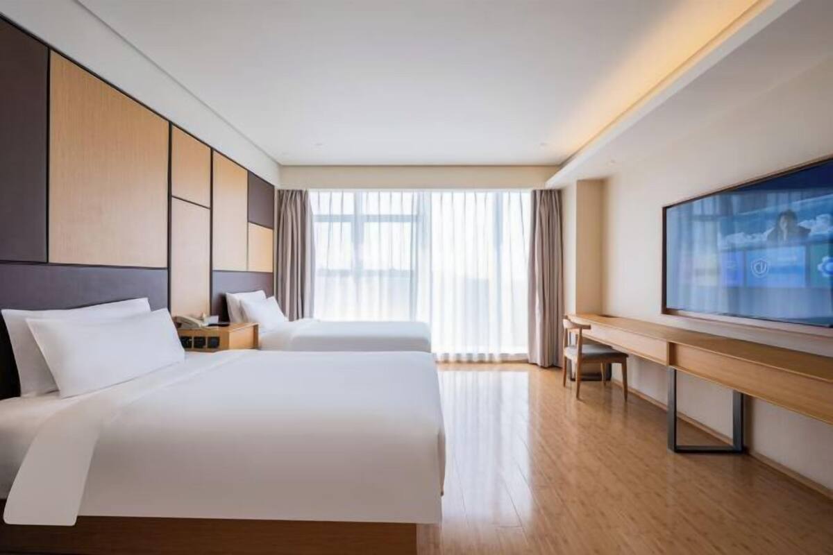 A hotel room with two beds, a TV, a desk, and a large window.