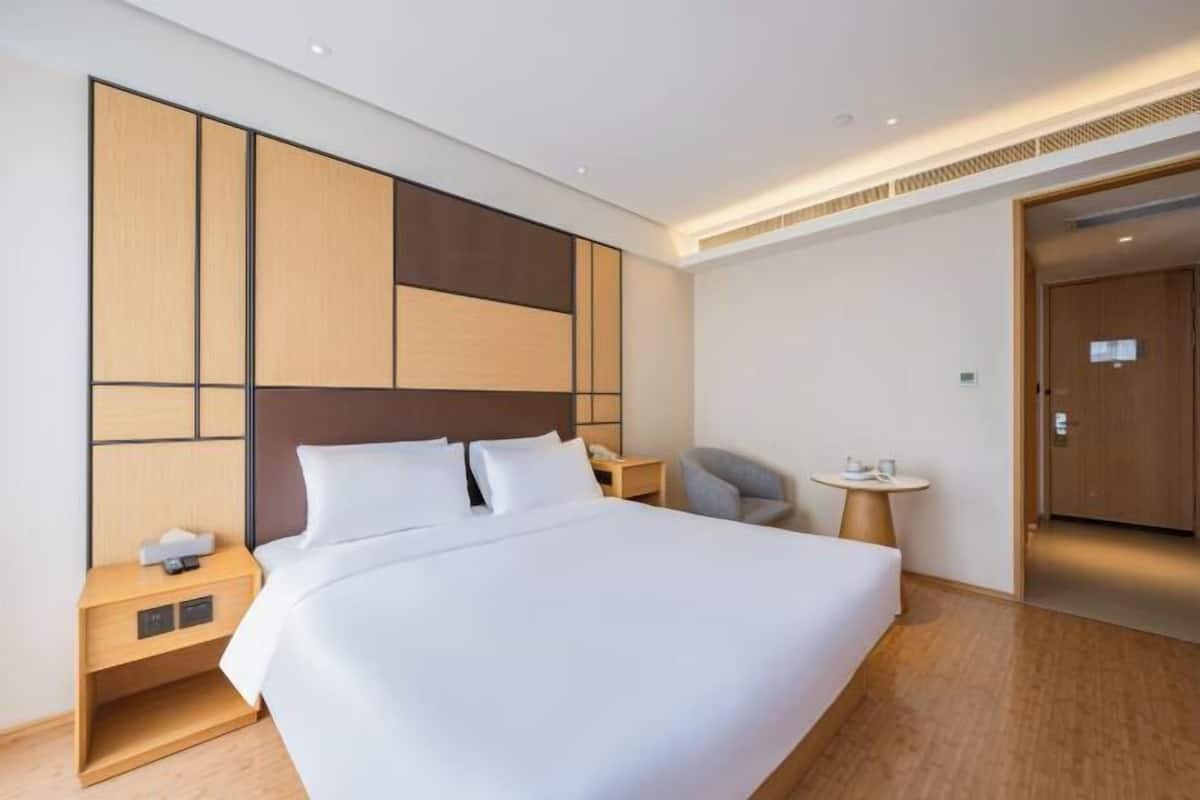A hotel room with a large bed, a nightstand, a chair, a small table, and a door.