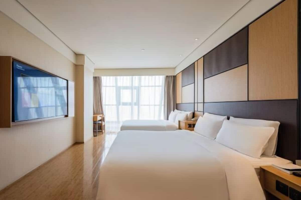 A hotel room with a large bed, a TV, and a window with curtains.