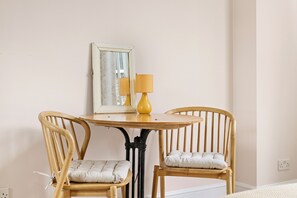 A room with a round wooden table, two wooden chairs with cushions, a mirror, and a yellow lamp.