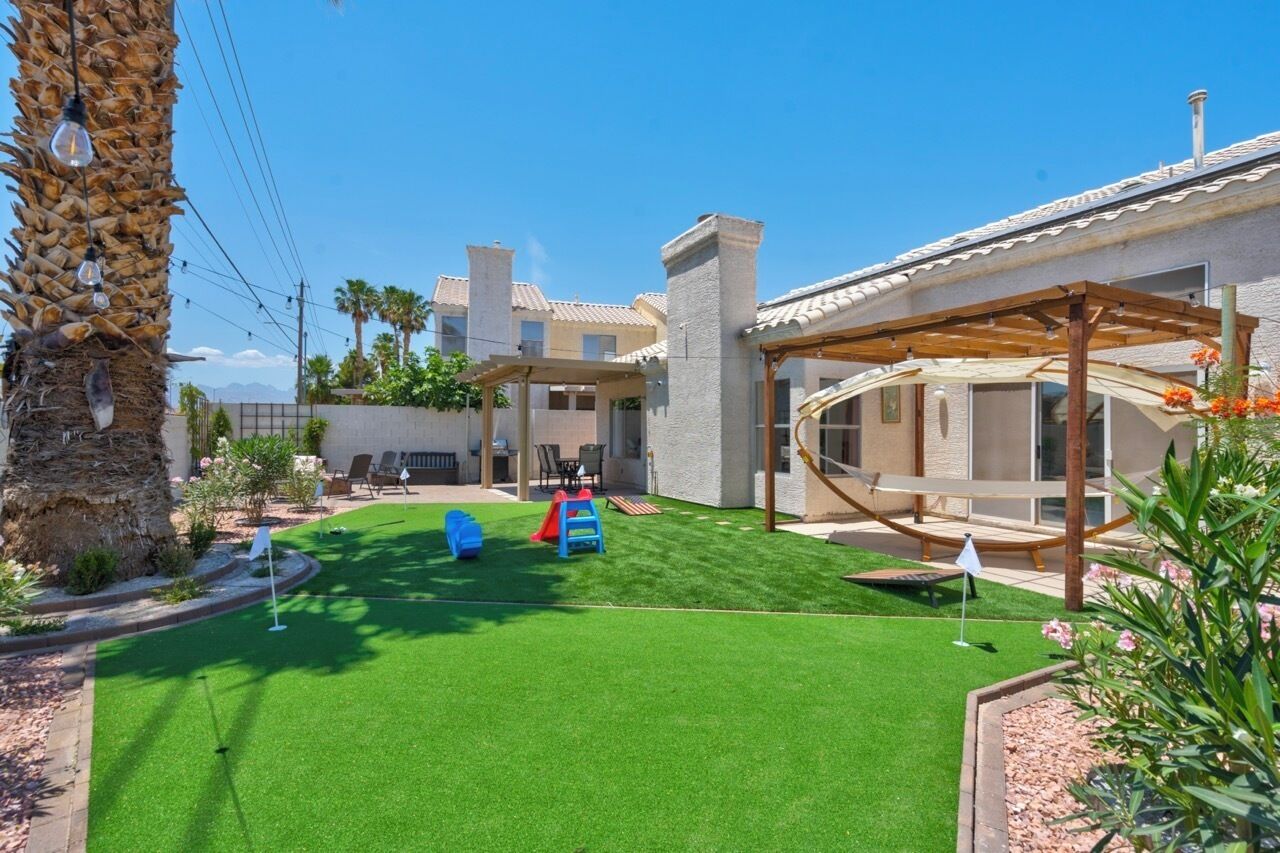 A backyard with artificial grass, a play area, and a pergola.