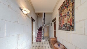 Un couloir avec un sol carrelé, un escalier aux marches décorées, un banc en bois et un tableau accroché au mur.