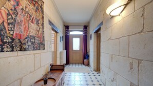 Un couloir doté d’un sol en mosaïque, d’une grande tapisserie sur le mur de gauche et d’un banc en bois avec un plateau.